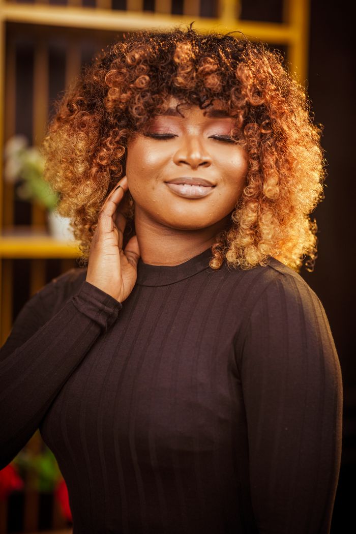 Portrait of a confident woman with curly afro hairstyle smiling indoors. Vibrant colors and warm lighting.