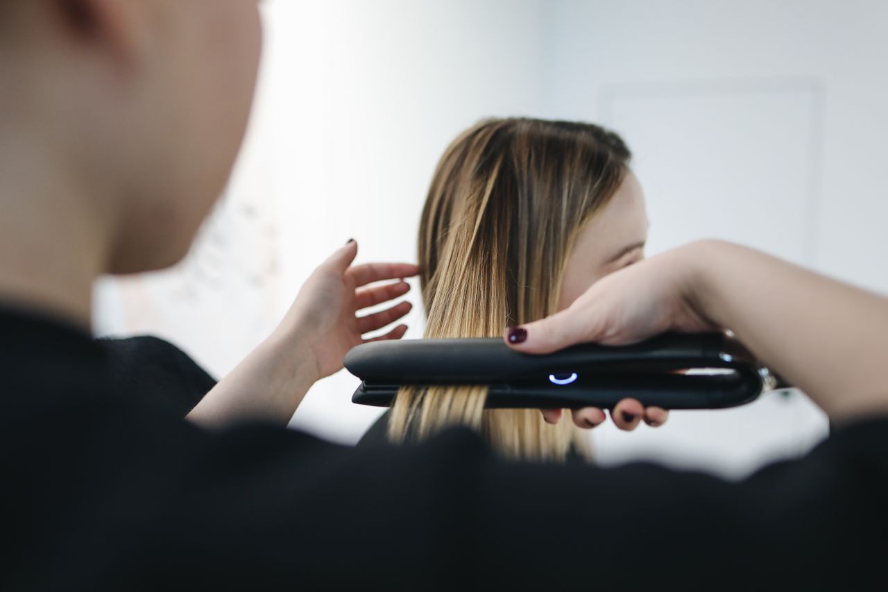 Close-up of a hairstylist using a straightening iron for sleek hairstyle indoors.